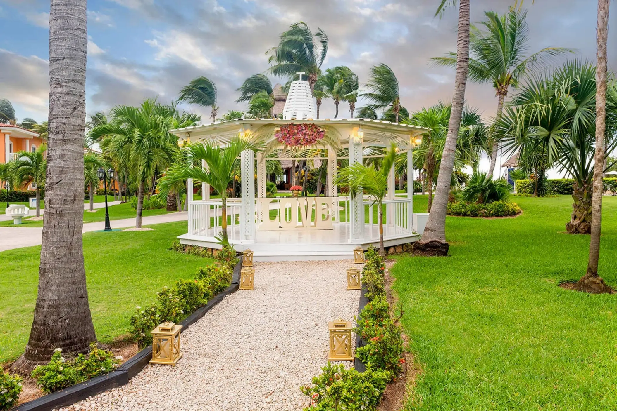 beautiful outdoor wedding gazebo on a lush green lawn, adorned with pink flowers and surrounded by palm trees