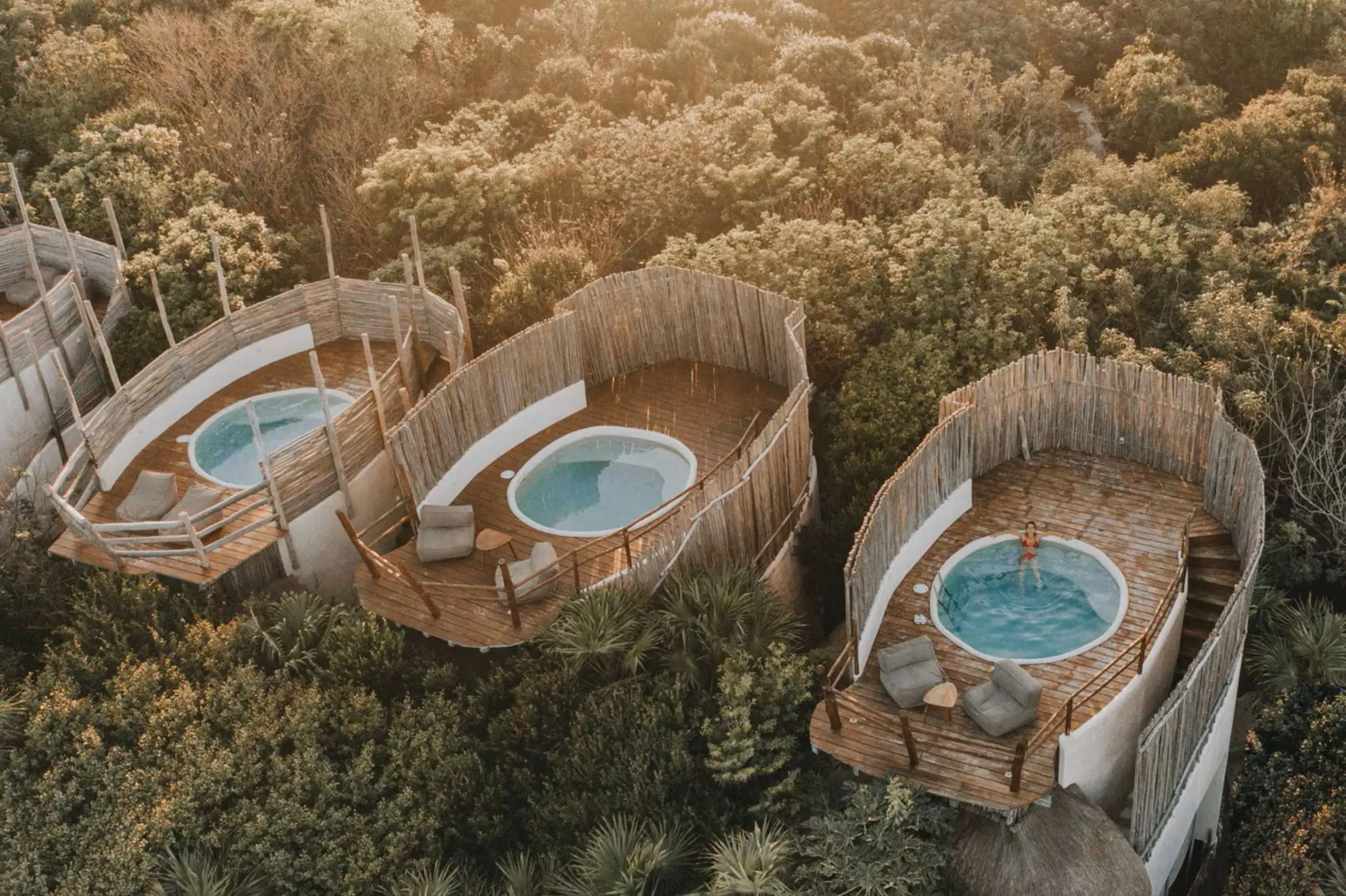 Aerial view of several unique casitas with circular plunge pools and wooden decks nestled within the lush jungle canopy.