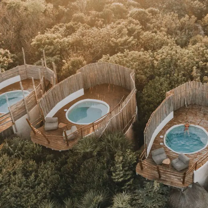 Aerial view of several unique casitas with circular plunge pools and wooden decks nestled within the lush jungle canopy.