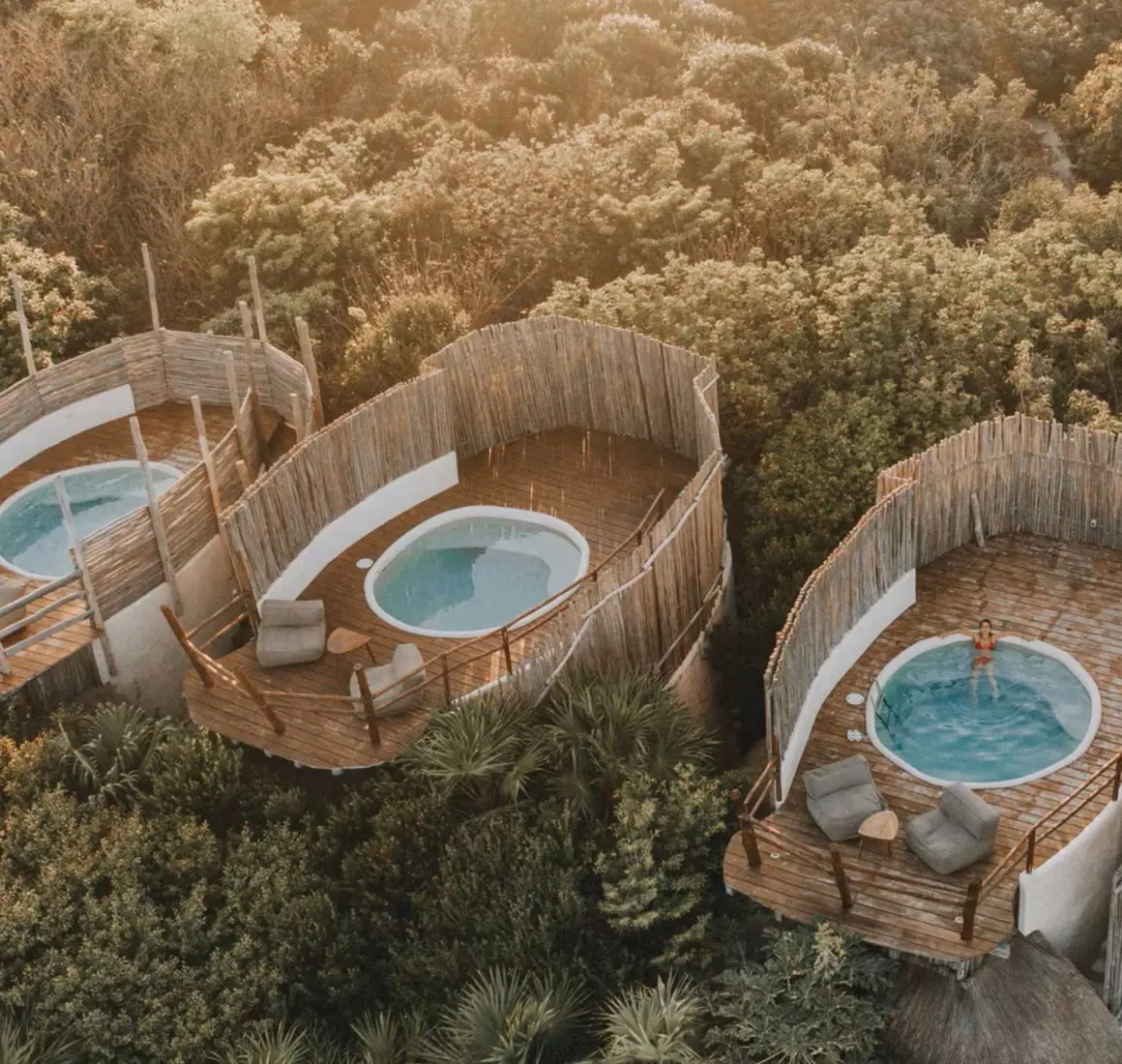 Aerial view of several unique casitas with circular plunge pools and wooden decks nestled within the lush jungle canopy.
