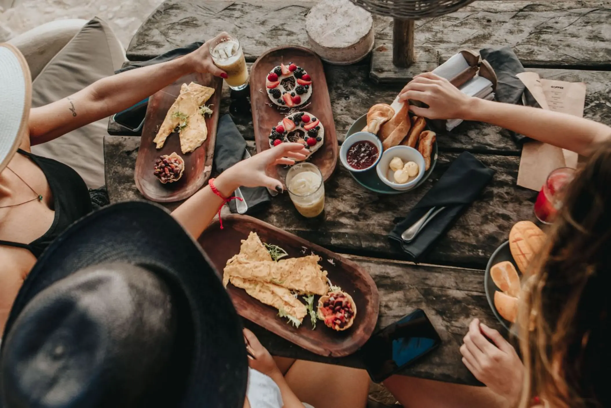 Overhead view of friends enjoying a delicious meal with fresh fruits, pastries, and drinks at a rustic wooden table at the resort restaurant.