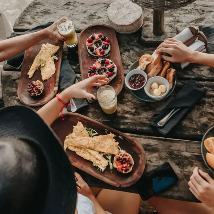 Overhead view of friends enjoying a delicious meal with fresh fruits, pastries, and drinks at a rustic wooden table at the resort restaurant.