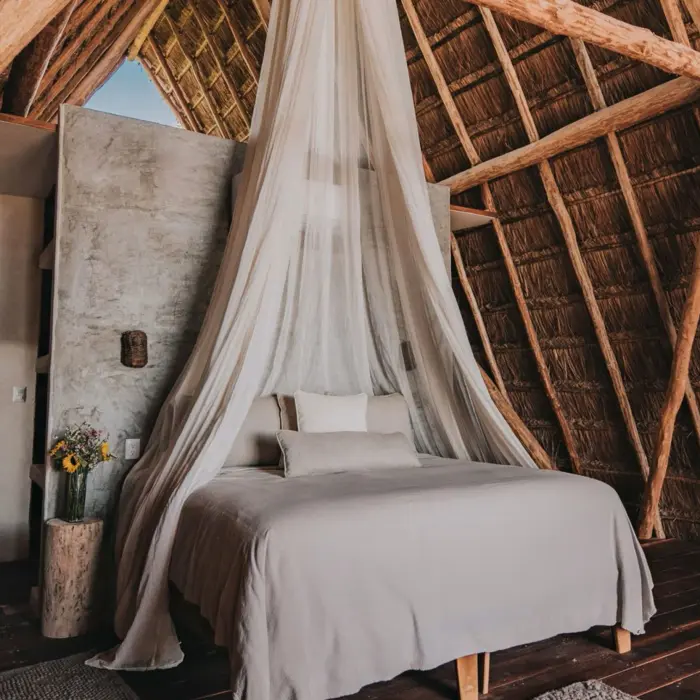 Interior of a loft with a high thatched roof, featuring a king bed draped in a white mosquito net and wooden floors.