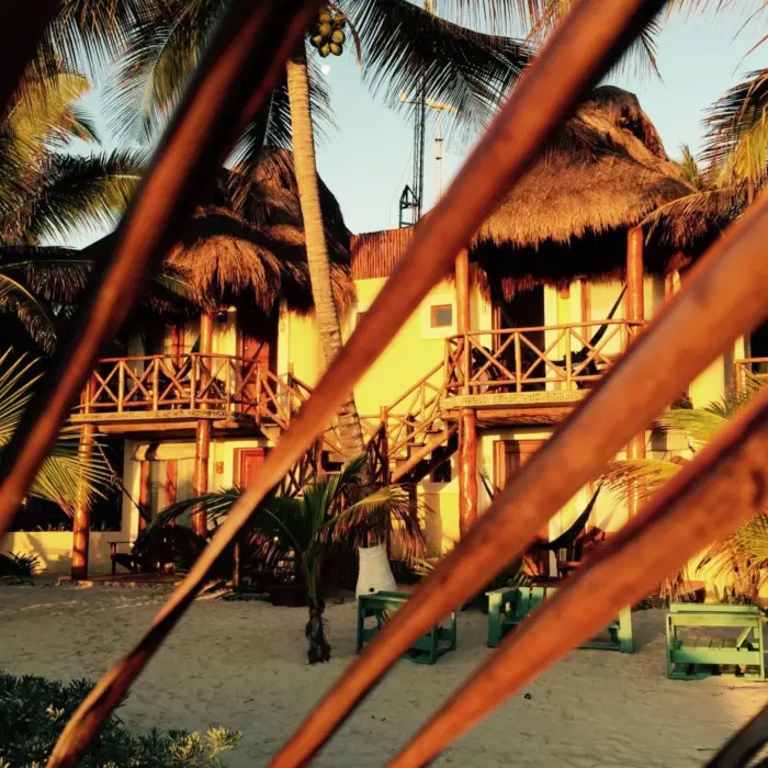 The exterior of guest accommodations at Piedra Escondida, featuring thatched roofs and balconies, nestled among palm trees.