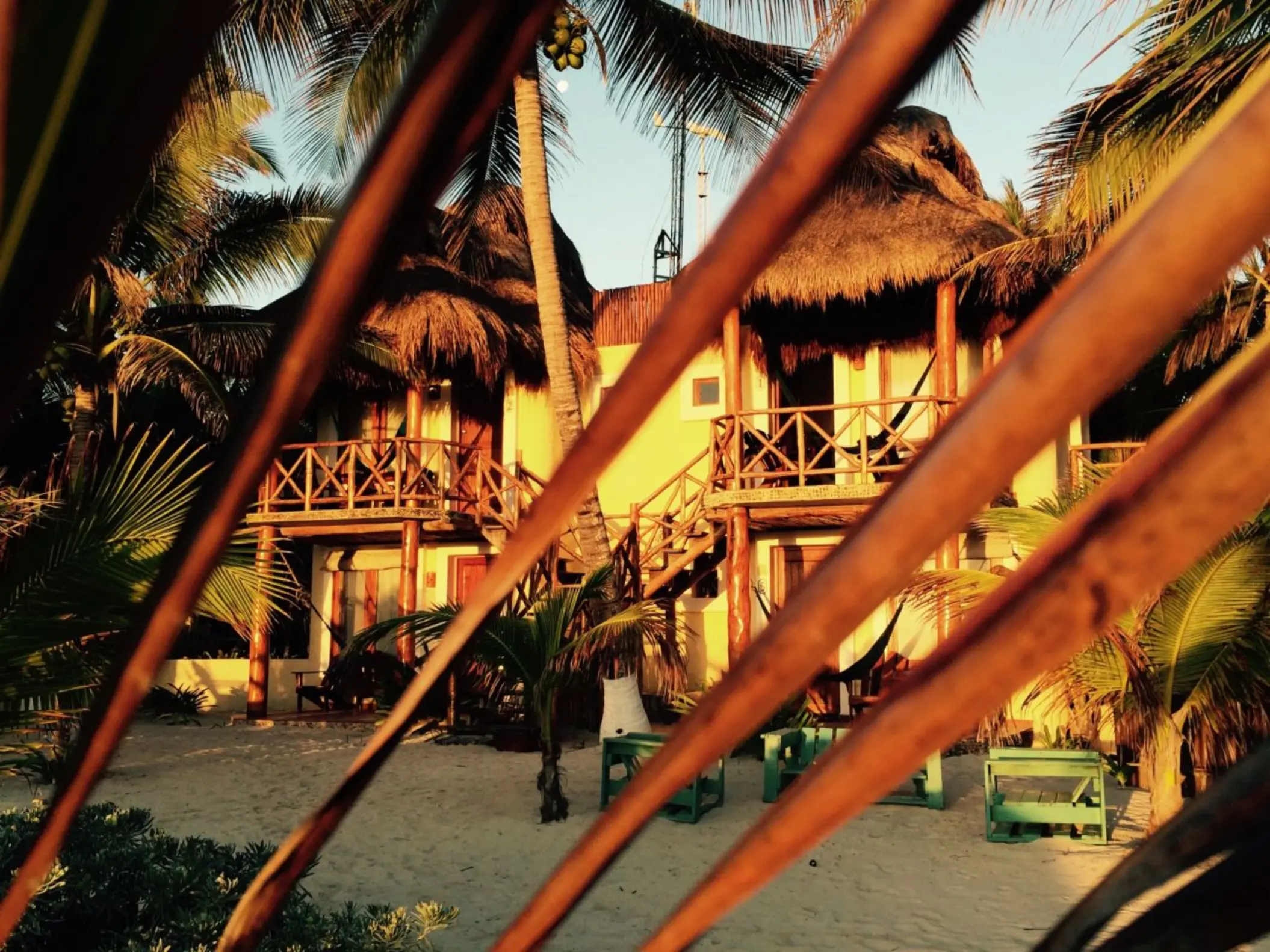 The exterior of guest accommodations at Piedra Escondida, featuring thatched roofs and balconies, nestled among palm trees.