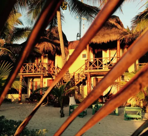 The exterior of guest accommodations at Piedra Escondida, featuring thatched roofs and balconies, nestled among palm trees.