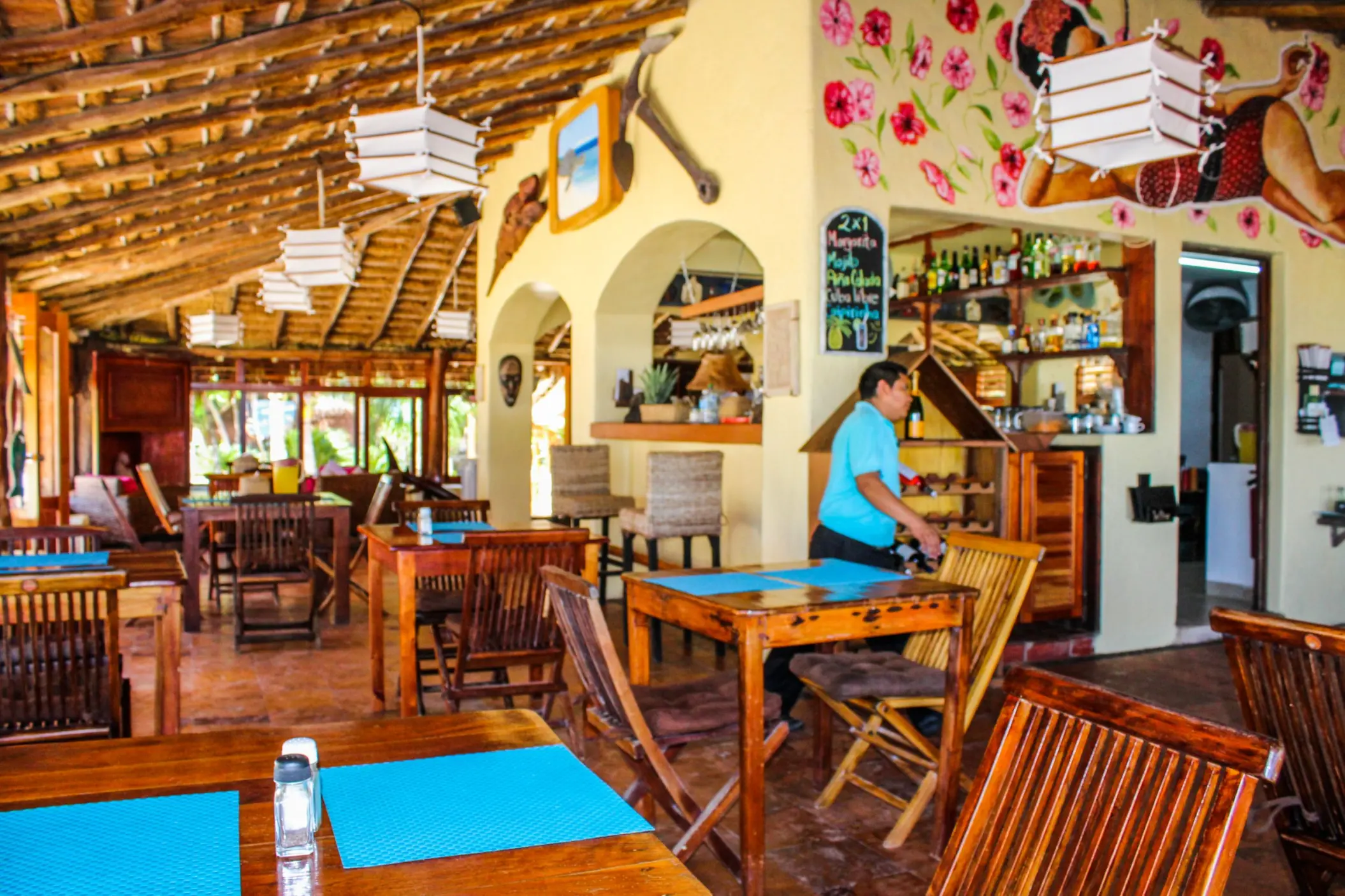 Interior of Restaurant Molcajete at Piedra Escondida with a thatched roof, wooden tables, a bar, and a server in a blue shirt.