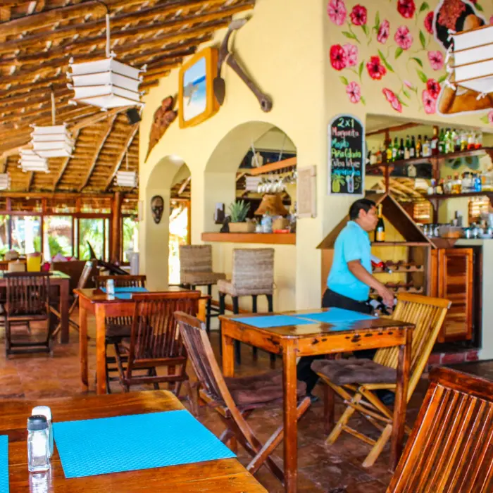 Interior of Restaurant Molcajete at Piedra Escondida with a thatched roof, wooden tables, a bar, and a server in a blue shirt.