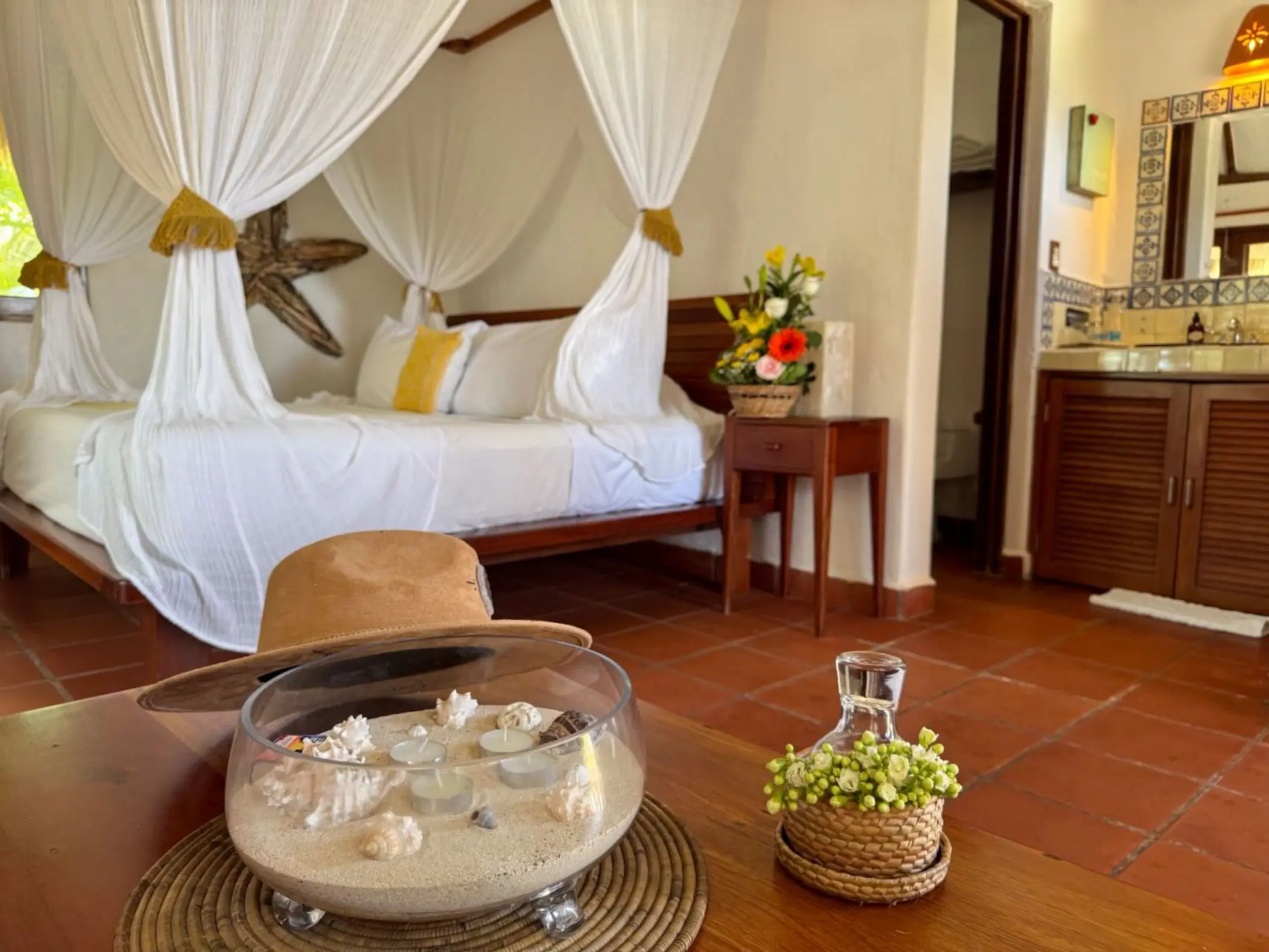 A cozy hotel room at Piedra Escondida with a four-poster bed draped in white, a decorative bowl, and a colorful sink.