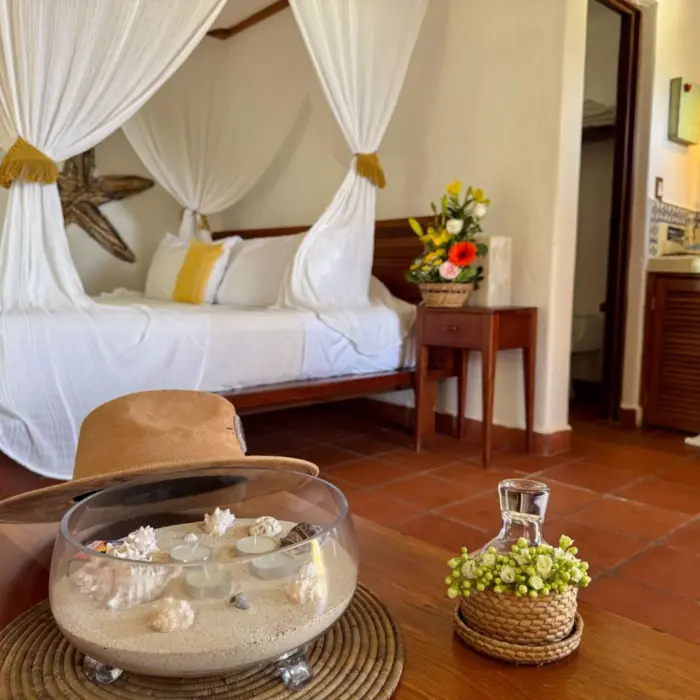 A cozy hotel room at Piedra Escondida with a four-poster bed draped in white, a decorative bowl, and a colorful sink.