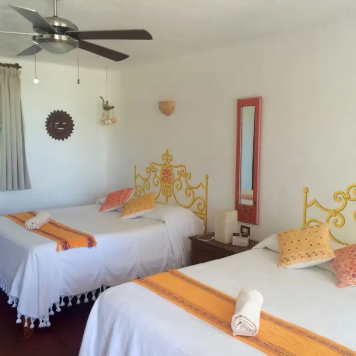 A vibrant hotel room at Piedra Escondida featuring two beds with colorful yellow and orange decorative accents and headboards.