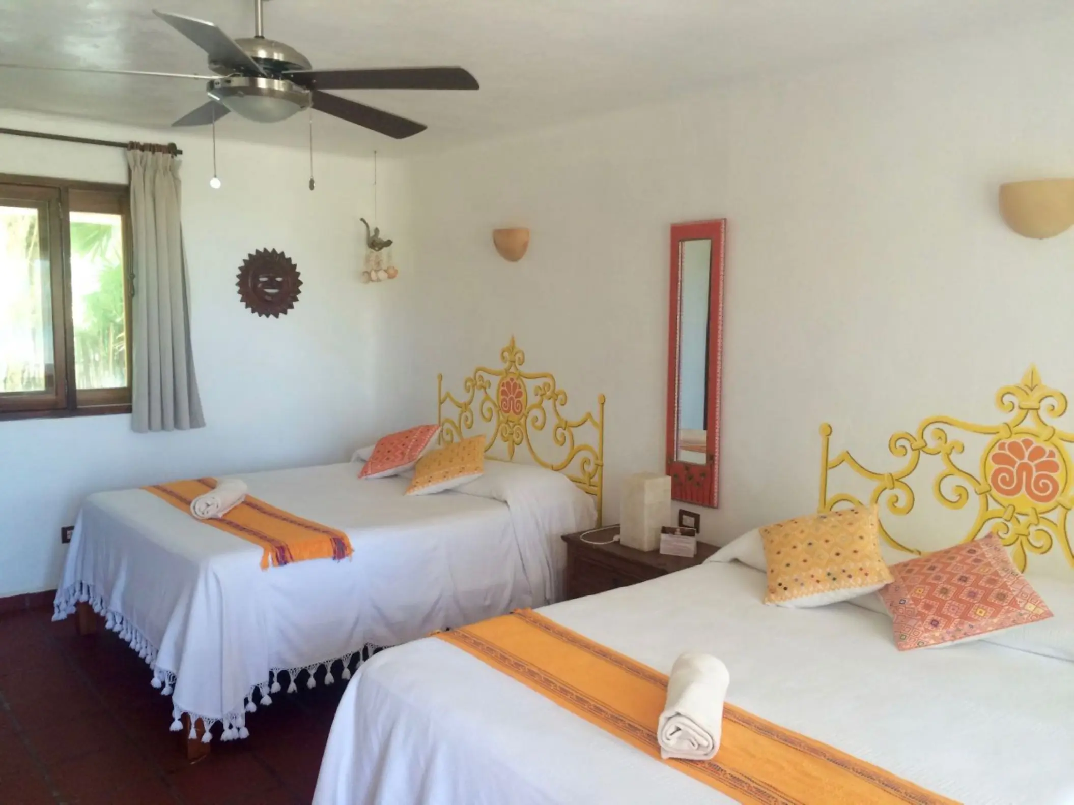 A vibrant hotel room at Piedra Escondida featuring two beds with colorful yellow and orange decorative accents and headboards.