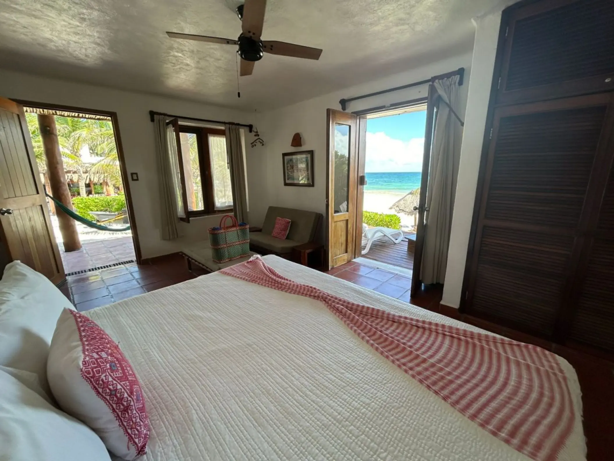 A bright hotel room at Piedra Escondida with a large bed, ceiling fan, and open doors leading to a balcony with an ocean view.