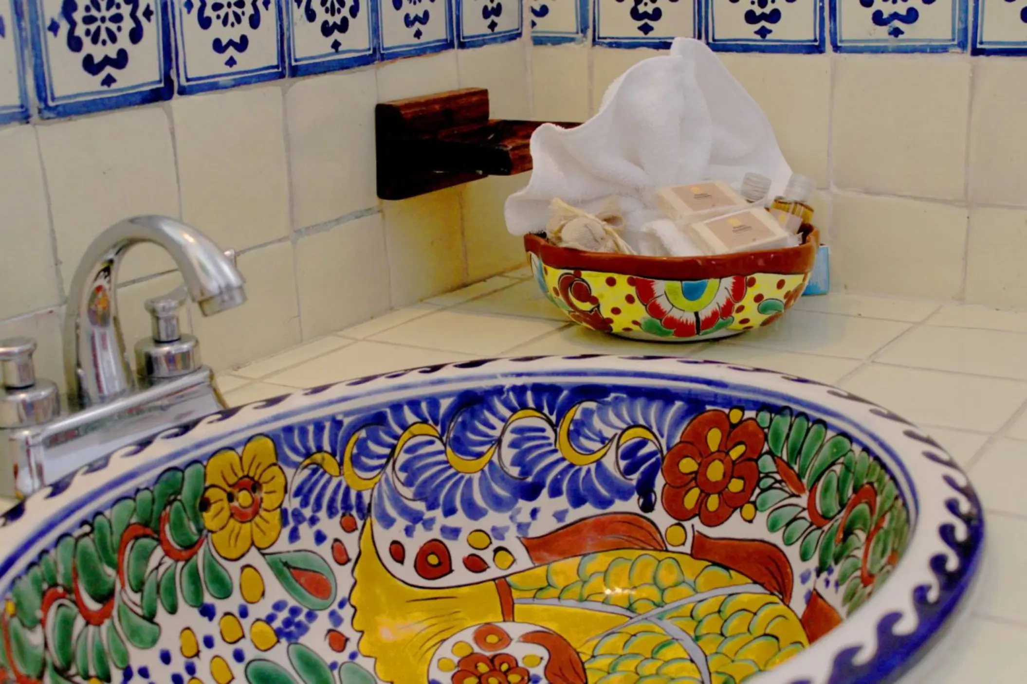A close-up of a colorful, hand-painted ceramic sink in a washroom at Piedra Escondida, with blue and white tiled walls.