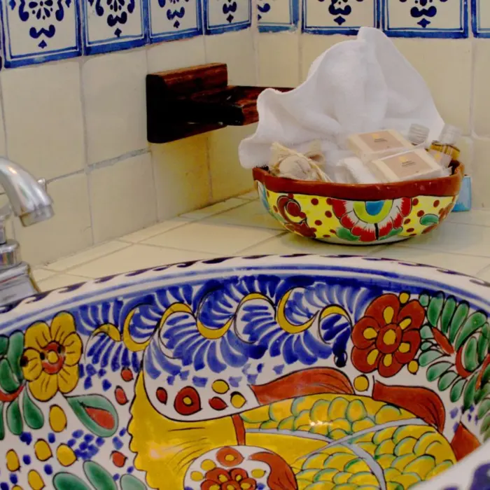 A close-up of a colorful, hand-painted ceramic sink in a washroom at Piedra Escondida, with blue and white tiled walls.