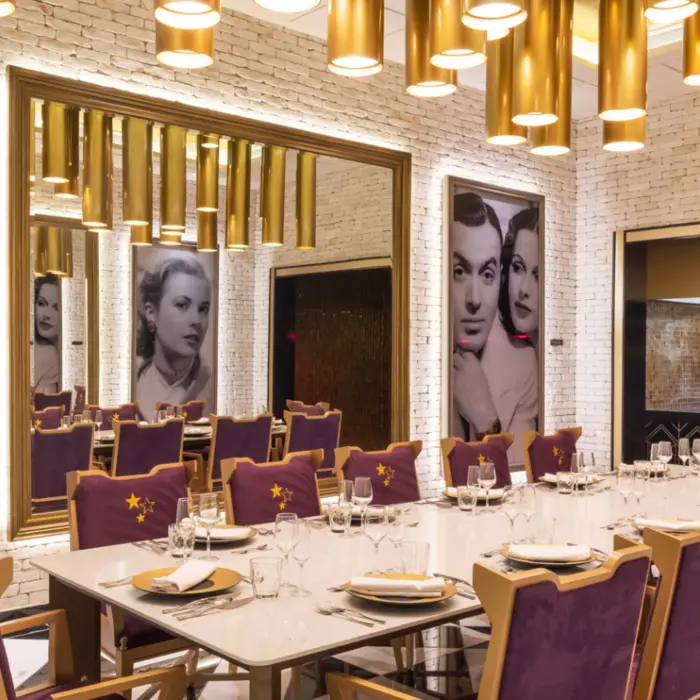 Elegant restaurant with gold lighting, vintage portraits, and purple velvet chairs set for a group dinner.