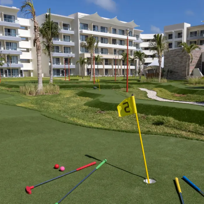 Mini-golf course with colorful putters on green turf, surrounded by palm trees and resort buildings.