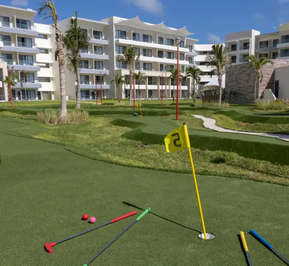 Mini-golf course with colorful putters on green turf, surrounded by palm trees and resort buildings.