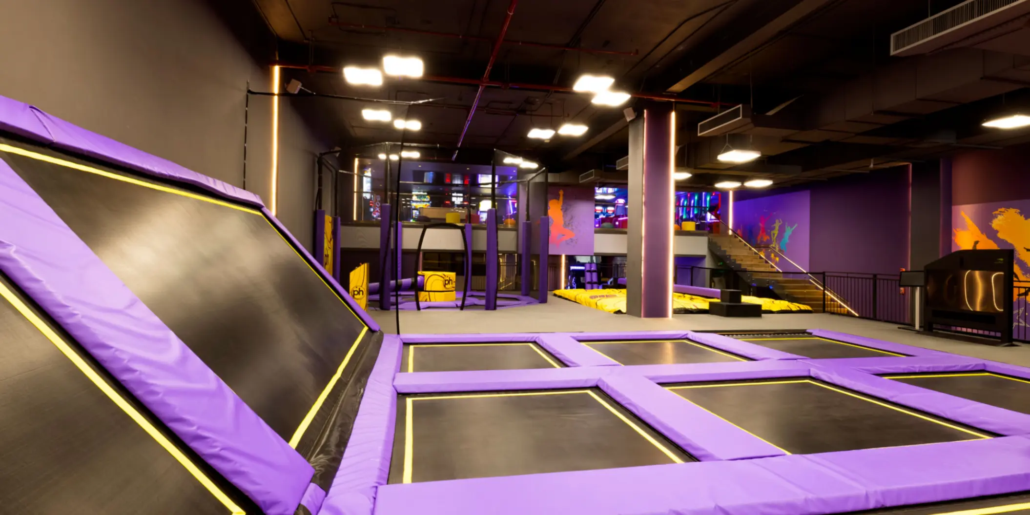 Indoor trampoline park with purple padding, climbing features, and vibrant lighting for active play.