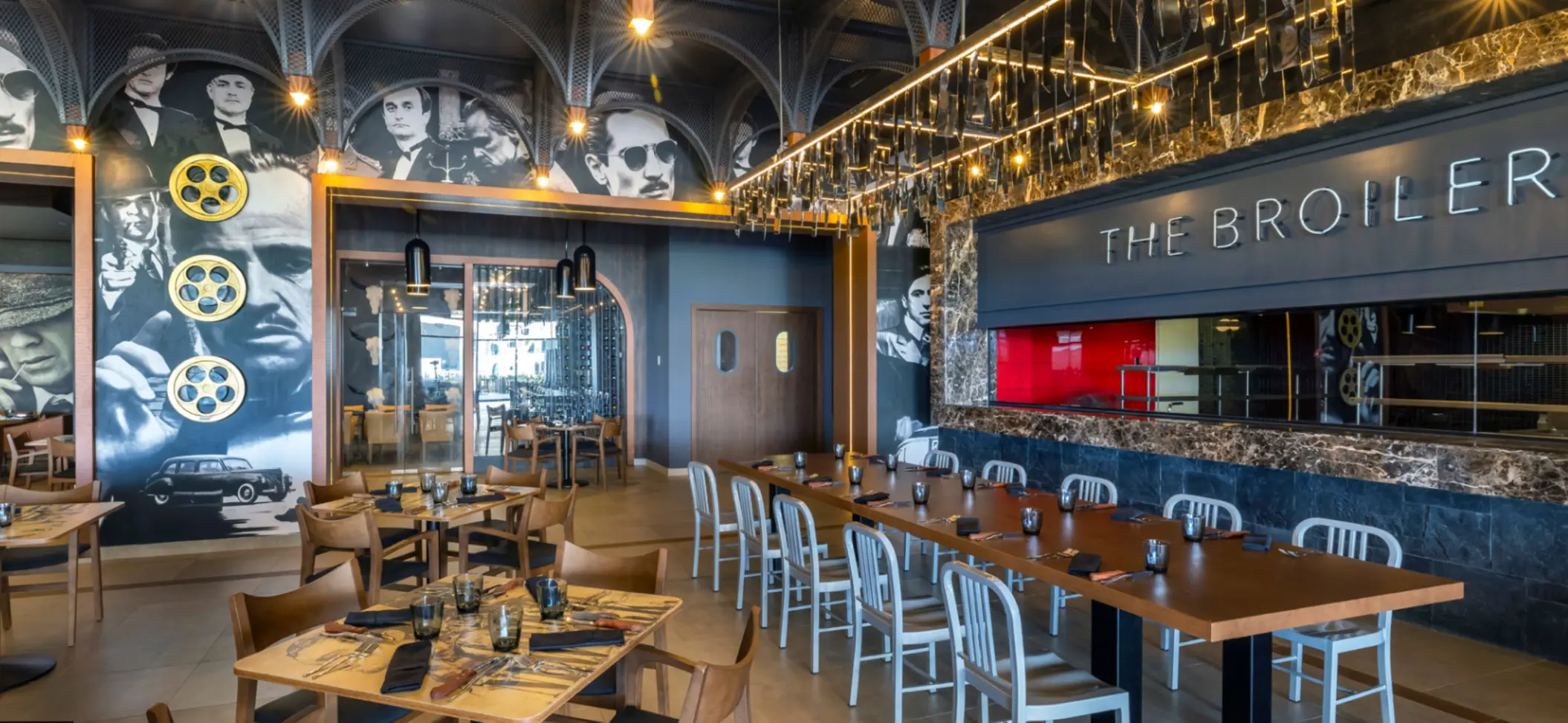 Movie-themed restaurant with black-and-white murals, wooden furniture, and “The Broiler” sign on wall.