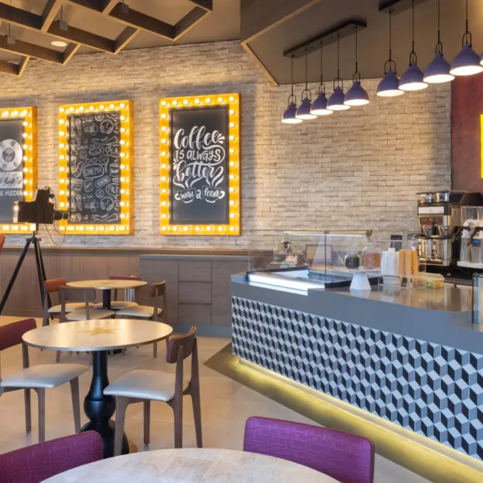 Trendy café with bright FUEL sign, dessert counter, indoor seating, and cinema-themed wall decorations.