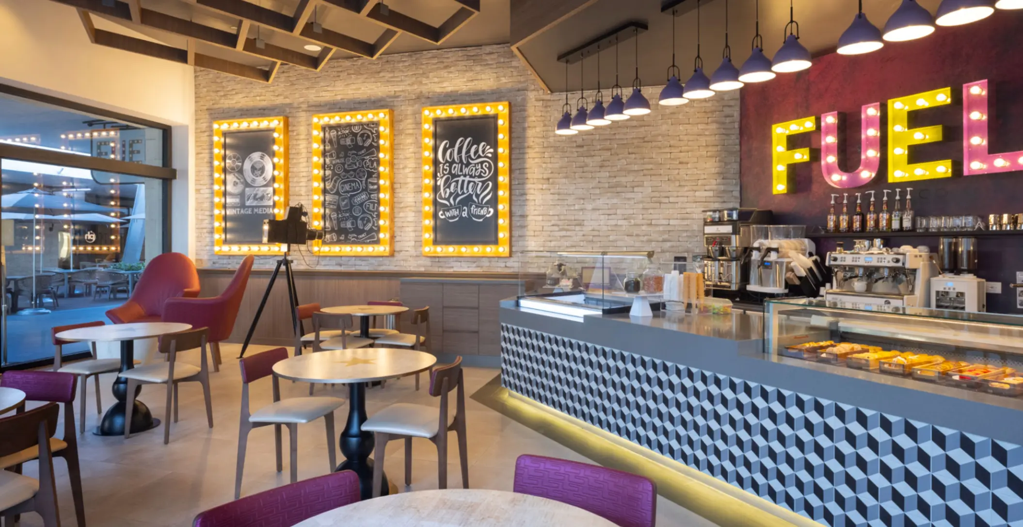 Trendy café with bright FUEL sign, dessert counter, indoor seating, and cinema-themed wall decorations.