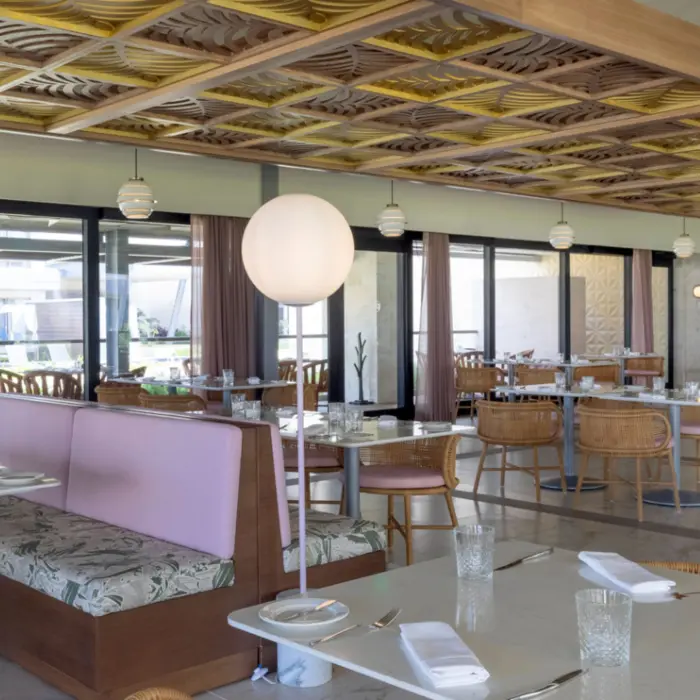 Bright, modern restaurant with rattan chairs, pastel booths, and large globe lights under a patterned ceiling.