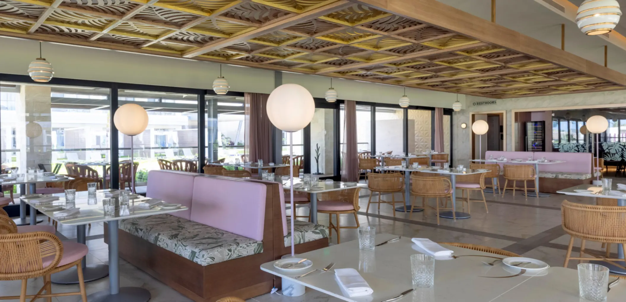 Bright, modern restaurant with rattan chairs, pastel booths, and large globe lights under a patterned ceiling.