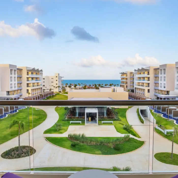 Balcony view of lush garden pathways leading to the ocean, surrounded by modern resort buildings and swim-up suites.