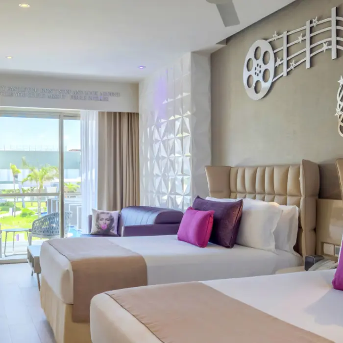 Modern resort room with double beds, balcony view, music-themed decor, and touches of purple and fuchsia pillows.