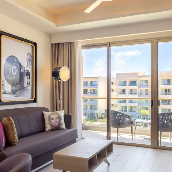 Living room with balcony, retro cinema artwork, and Marilyn Monroe pillow at a stylish all-inclusive resort suite.