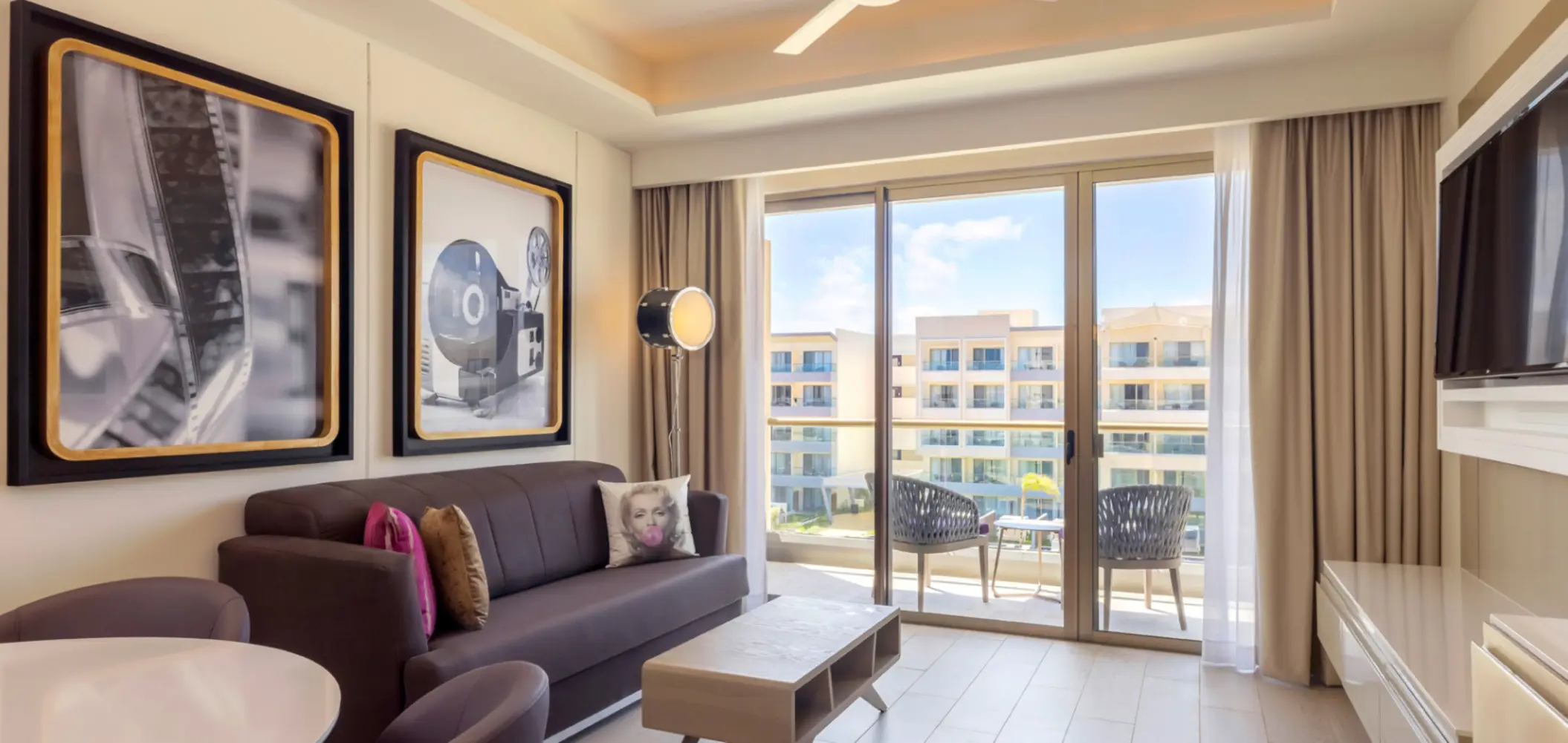 Living room with balcony, retro cinema artwork, and Marilyn Monroe pillow at a stylish all-inclusive resort suite.