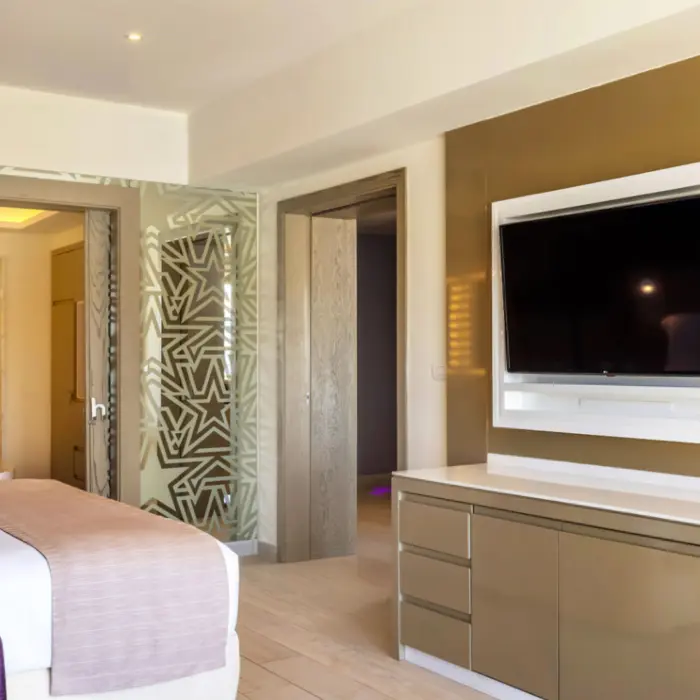 Spacious resort suite with gold accent wall, large TV, and freestanding soaking tub visible through glass panels.