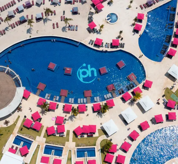 Aerial view of resort pools, pink umbrellas, beach loungers, and cabanas arranged around a central lagoon-style pool.