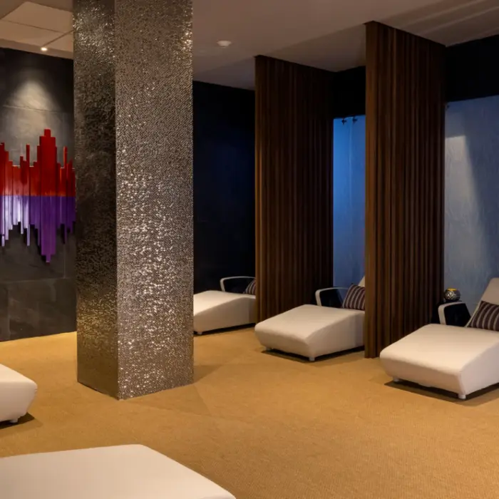 Tranquil spa lounge with white chaise chairs, mood lighting, and modern art on dark slate walls.