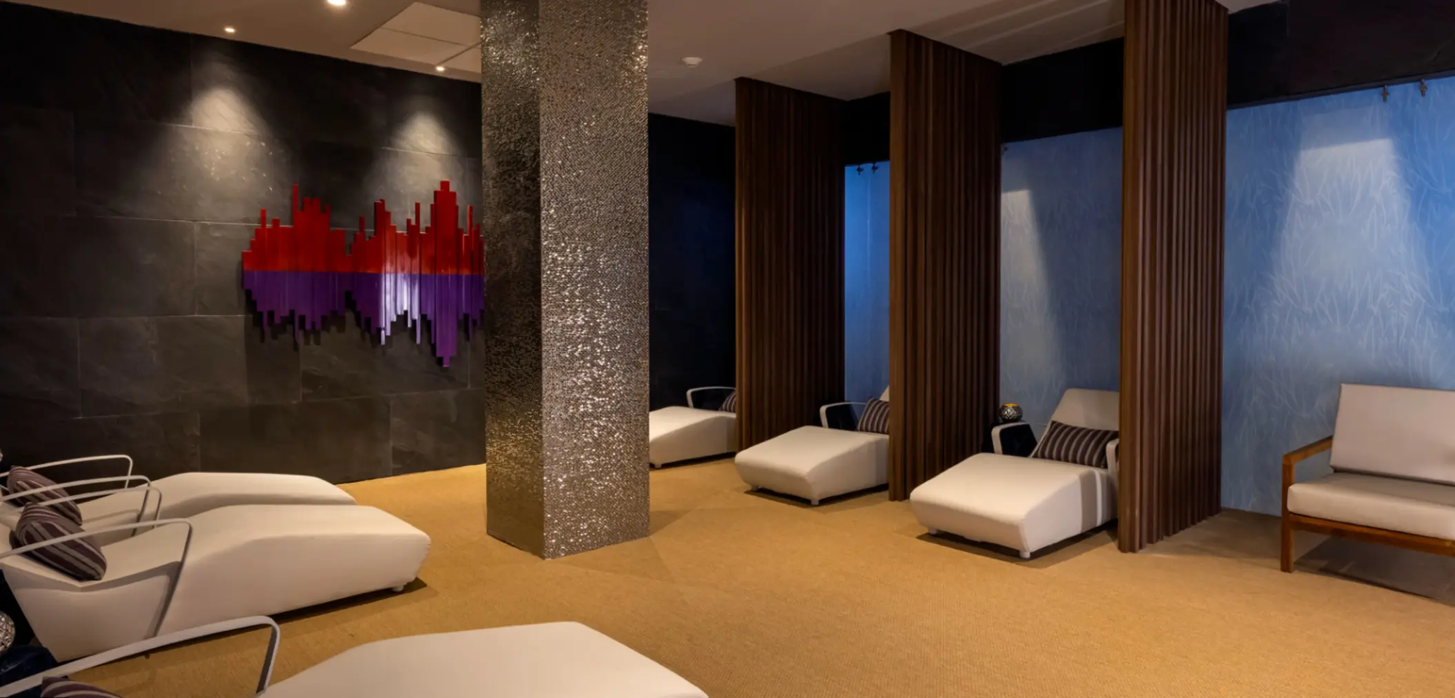 Tranquil spa lounge with white chaise chairs, mood lighting, and modern art on dark slate walls.