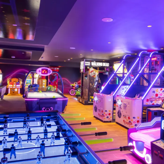 Vibrant arcade room with neon lights, foosball, air hockey, and popular games in a family-friendly resort space.