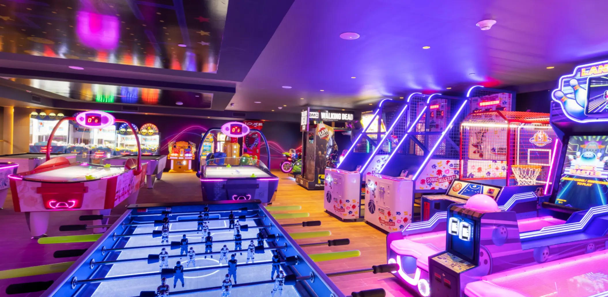 Vibrant arcade room with neon lights, foosball, air hockey, and popular games in a family-friendly resort space.
