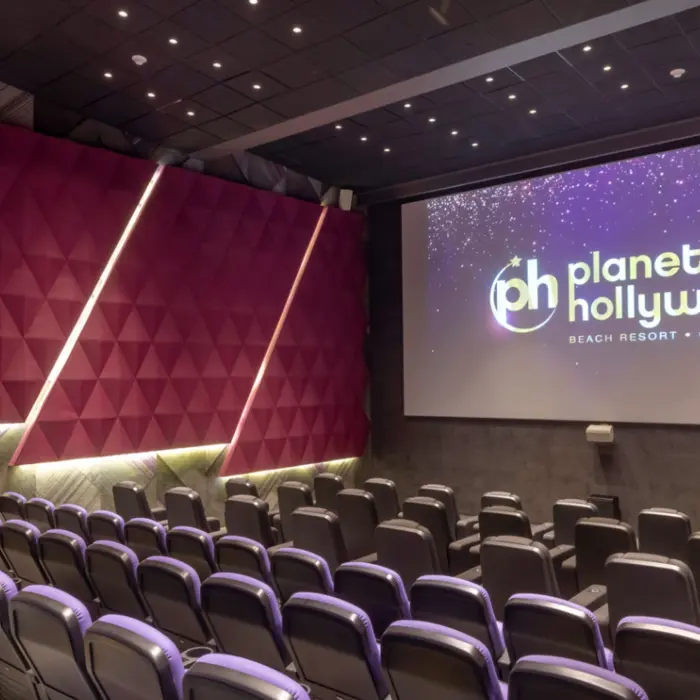 Resort movie theater with plush seats, purple walls, and large screen displaying the Planet Hollywood logo.