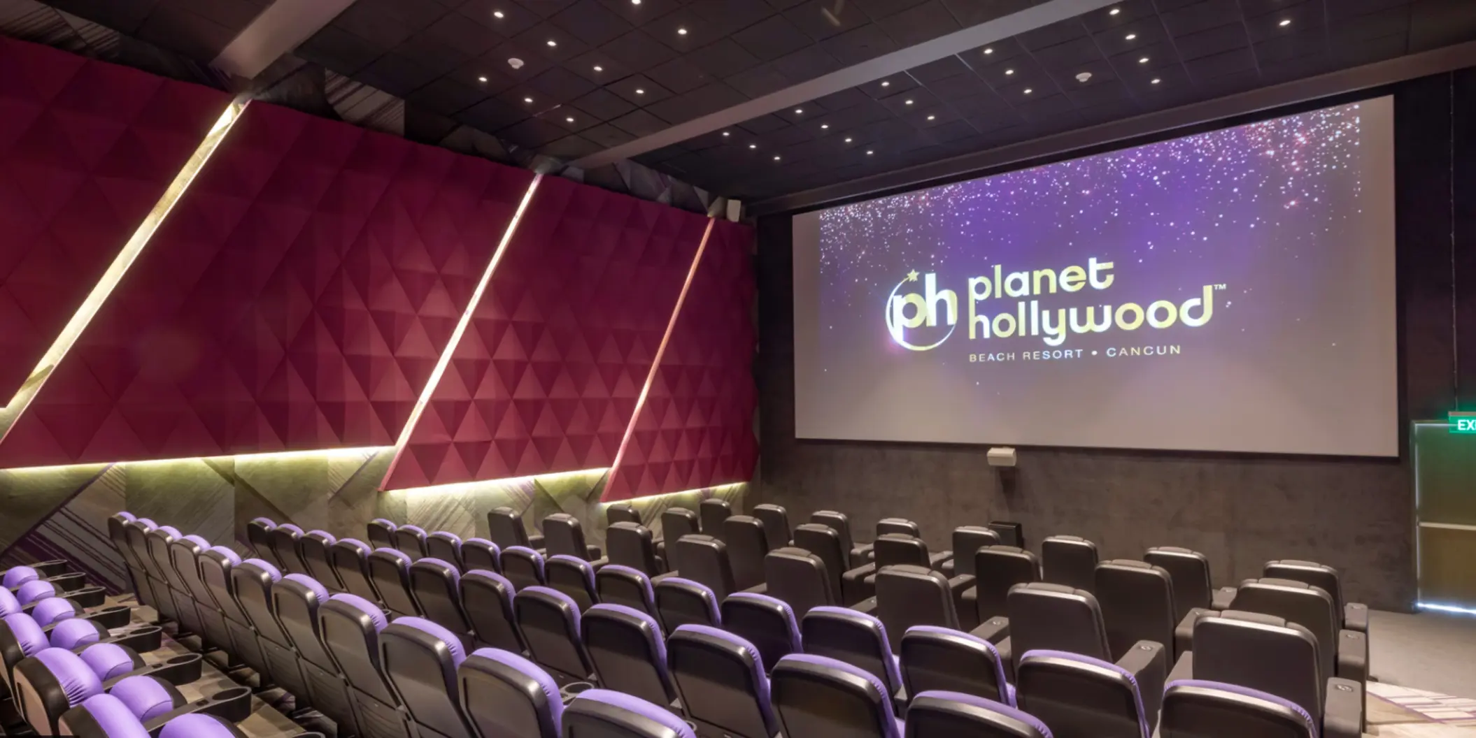 Resort movie theater with plush seats, purple walls, and large screen displaying the Planet Hollywood logo.