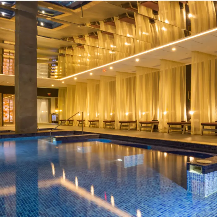 Indoor hydrotherapy pool surrounded by soft lighting, sheer curtains, and lounge chairs in an elegant spa setting.