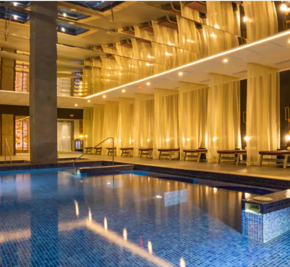 Indoor hydrotherapy pool surrounded by soft lighting, sheer curtains, and lounge chairs in an elegant spa setting.