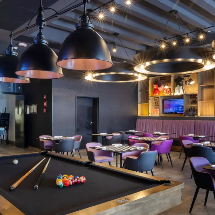 Trendy sports bar with modern decor, game tables, large TV screens, and purple-lit bar counter seating.
