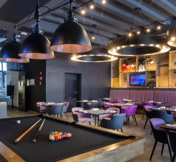 Trendy sports bar with modern decor, game tables, large TV screens, and purple-lit bar counter seating.
