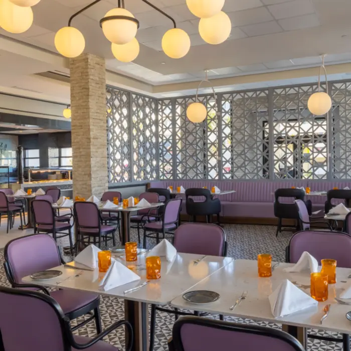 Bright dining room with purple chairs, globe lights, and orange glassware in a casual, airy resort restaurant.