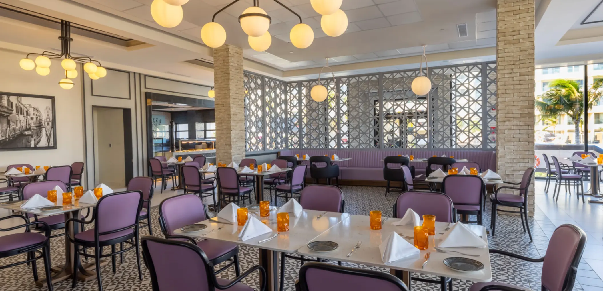 Bright dining room with purple chairs, globe lights, and orange glassware in a casual, airy resort restaurant.