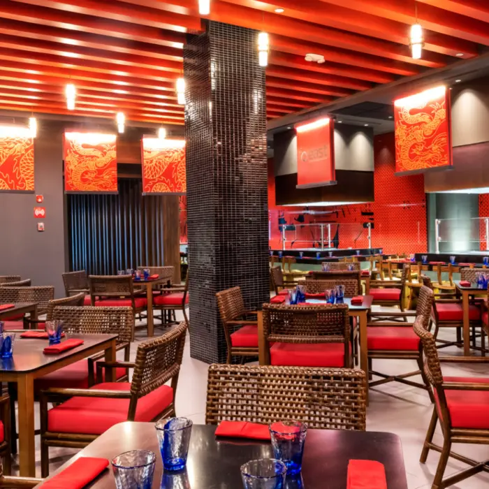Asian restaurant with red decor, woven chairs, modern teppanyaki setup, and dragon-themed artwork on the walls.