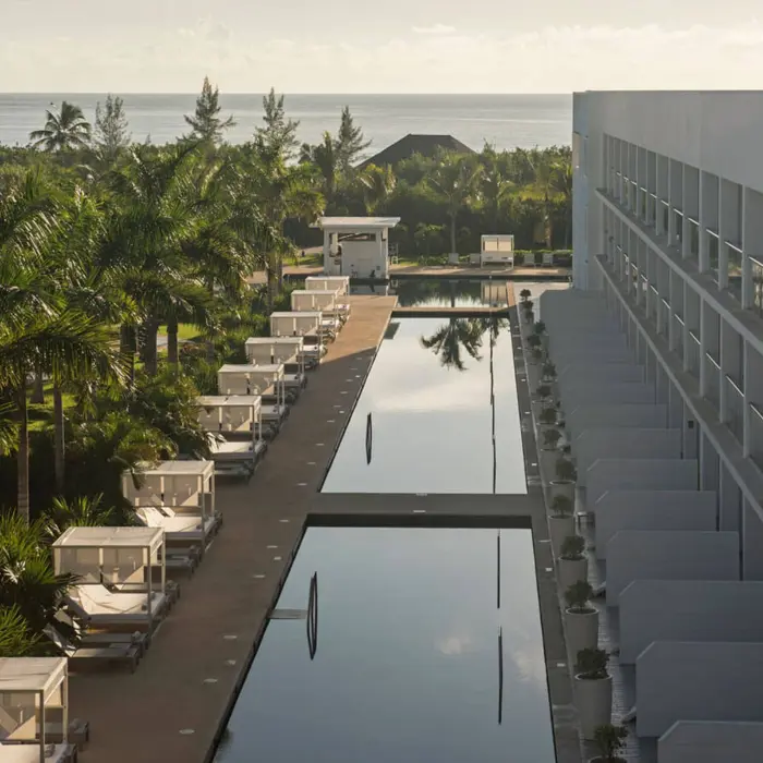 View of the Platinum Yucatan Princess swim-out suites exterior, showing a long pool flanked by palm trees and hotel buildings.