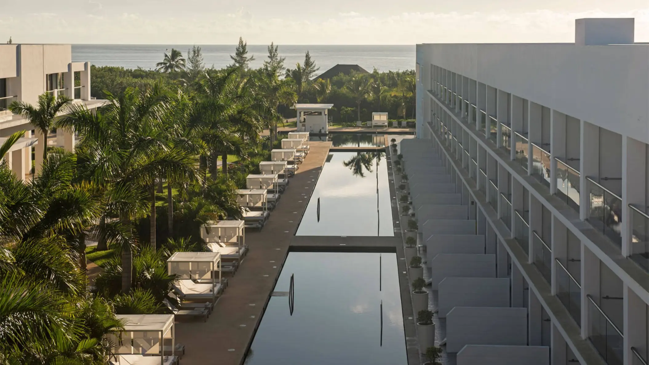 View of the Platinum Yucatan Princess swim-out suites exterior, showing a long pool flanked by palm trees and hotel buildings.