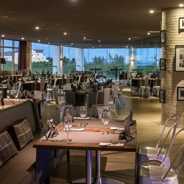 Interior of a hotel restaurant with modern decor, a large decorative bicycle, and floor-to-ceiling windows overlooking the ocean.